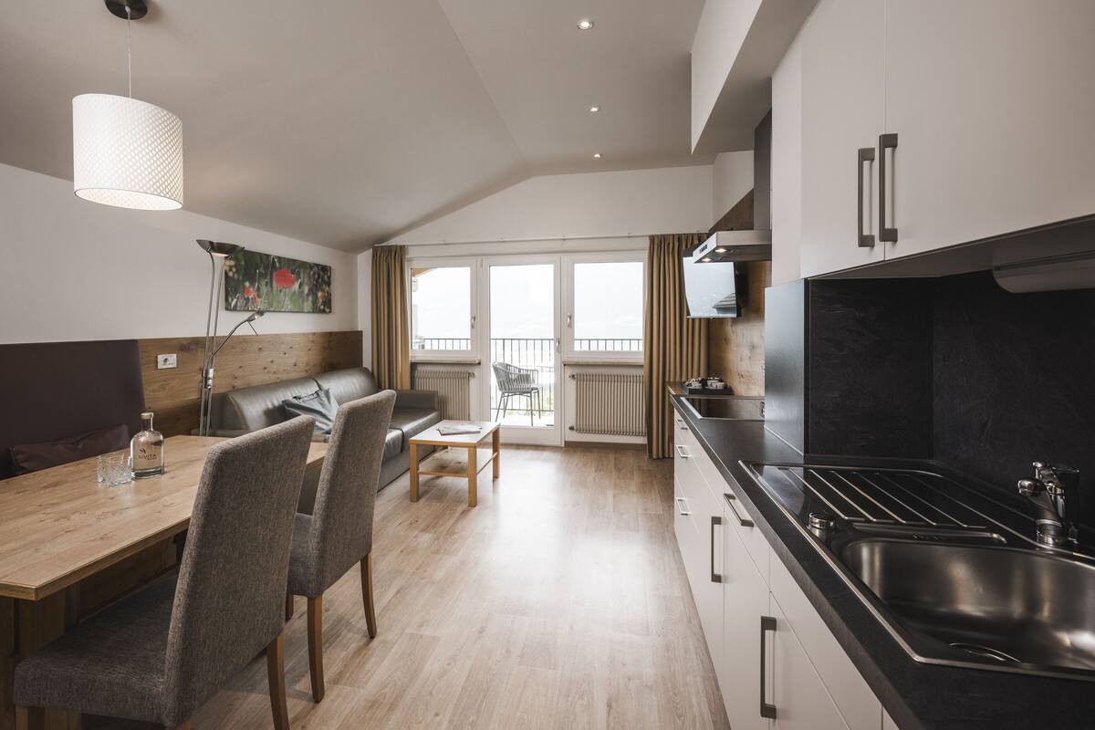 A modern kitchen with a black stove, white cabinets, and a wooden dining table with chairs.