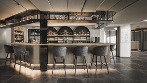 Zona de bar moderna con barra central, diversas opciones de asientos y una escalera que lleva a niveles superiores.
