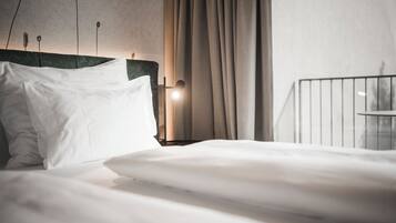 Een net opgemaakt bed met witte lakens, een met groen bekleden hoofdeinde en een bedlampje.