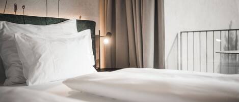 A neatly made bed with white linens, a green upholstered headboard, and a bedside lamp.