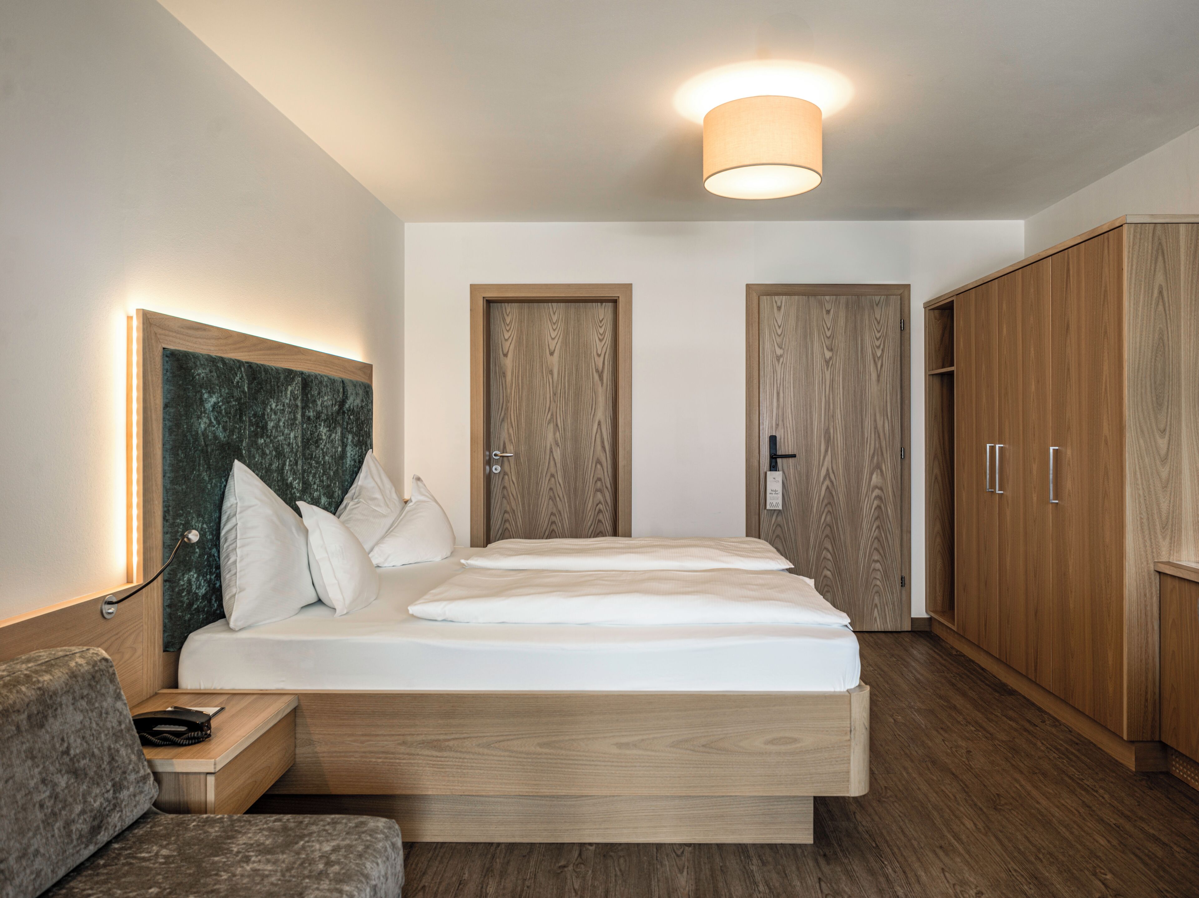 A modern bedroom with a wooden bed, a nightstand, a headboard, and a wardrobe.