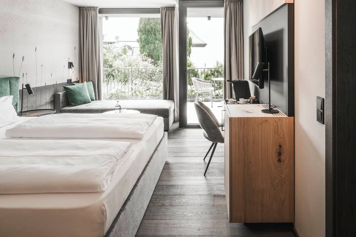A modern hotel room with two beds, a desk, and a TV.