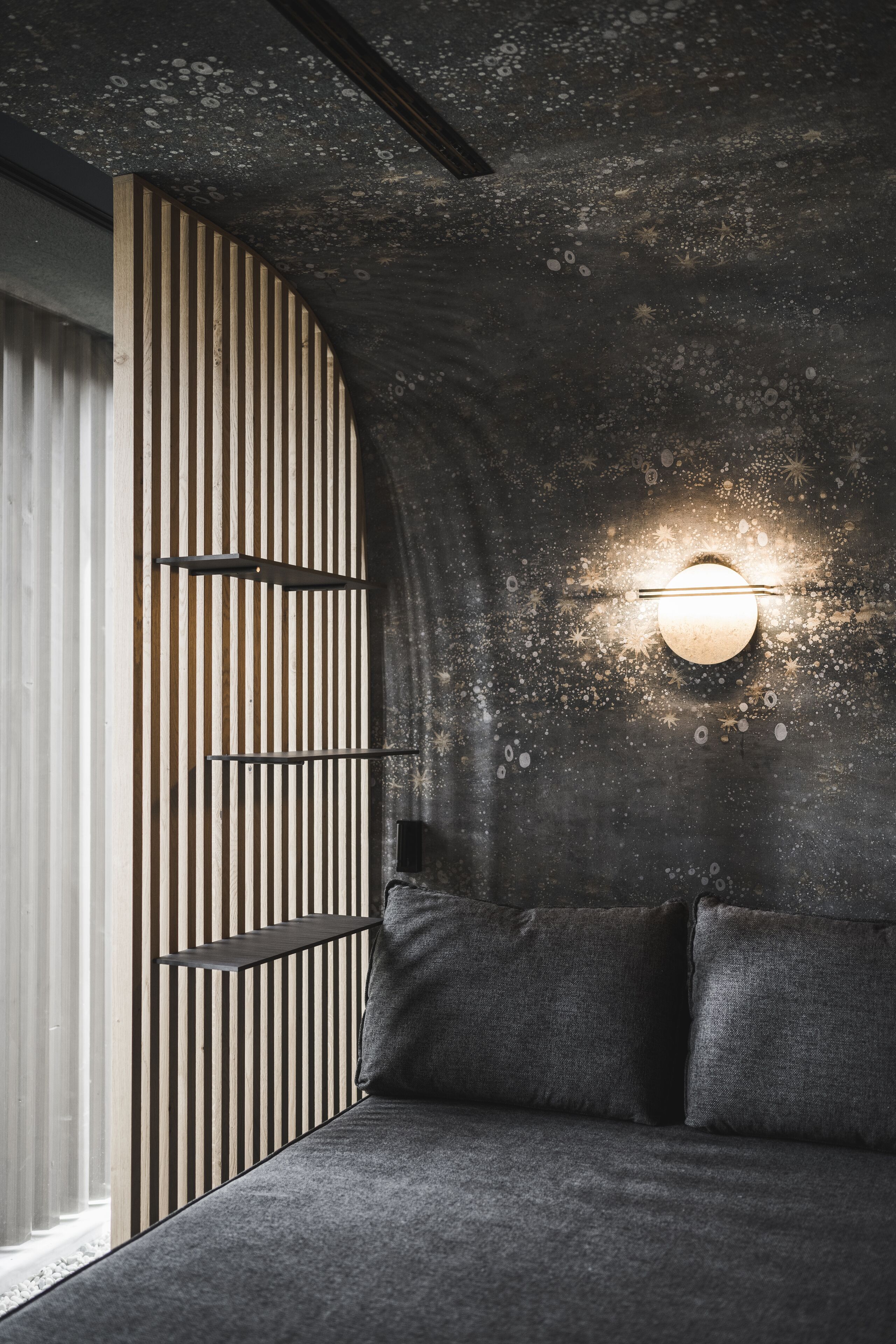 Una camera moderna con soffitto curvo, una lampada a parete e un divano con cuscini.
