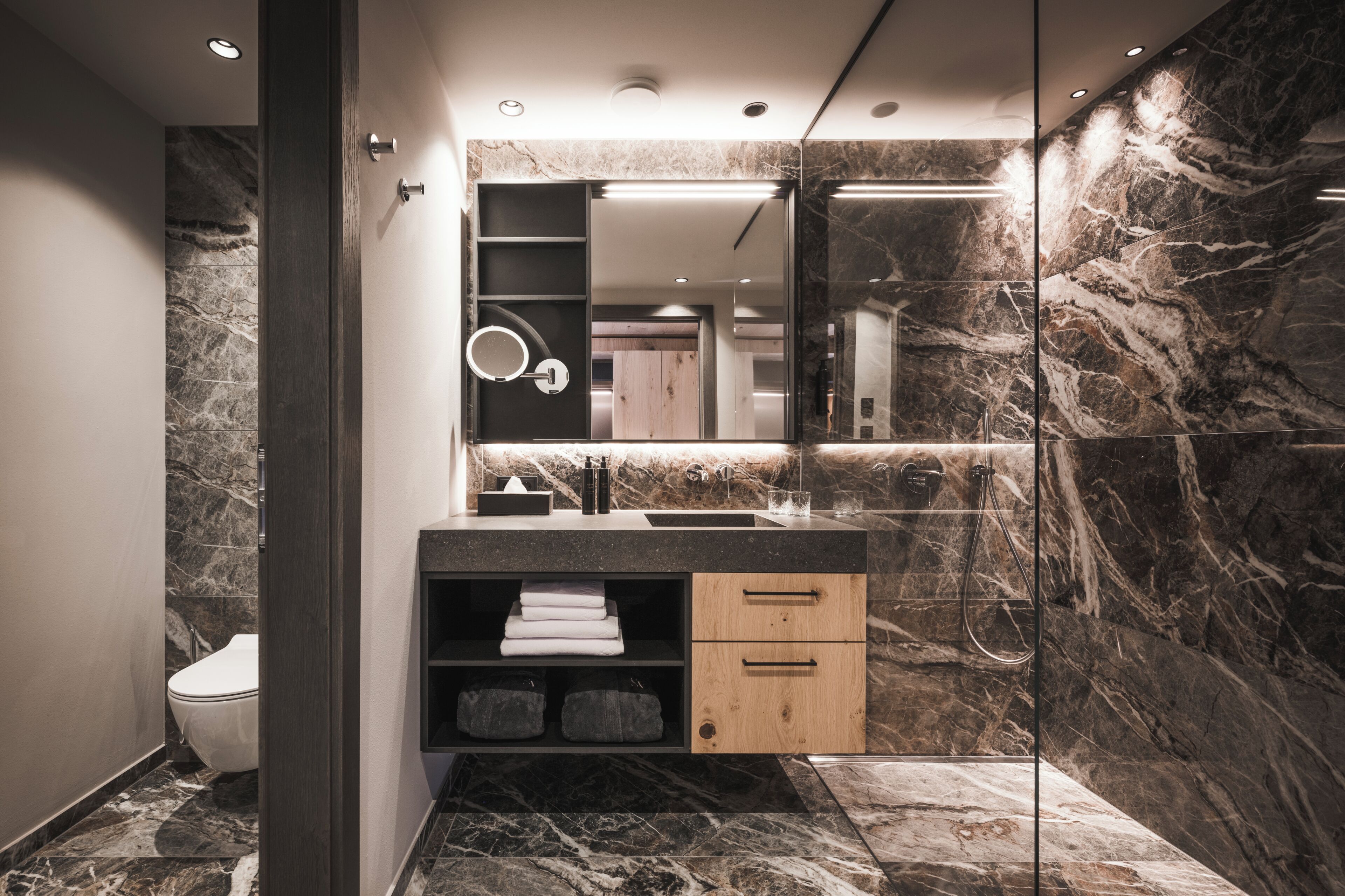 Un baño moderno con piso de mármol, lavamanos integrado, espejo y retrete.
