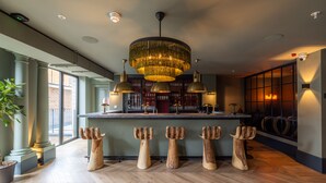 A bar area with a central chandelier, wooden stools, and a bar counter.