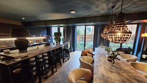 A modern kitchen with a bar area, large windows, and a chandelier.