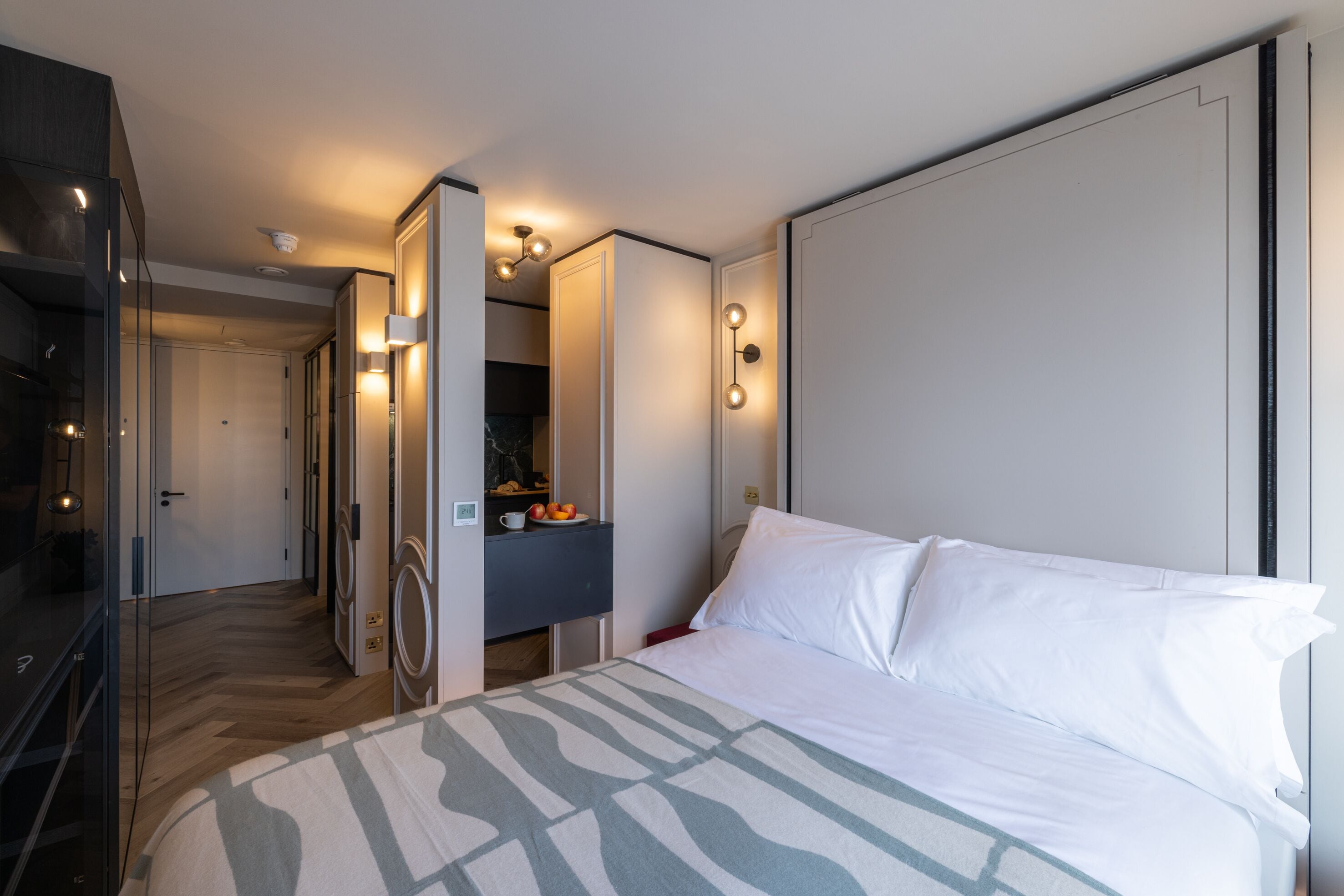 Ett modernt hotellrum med en stor säng, en inbyggd garderob, en sminkbord med spegel och ett litet pentry.