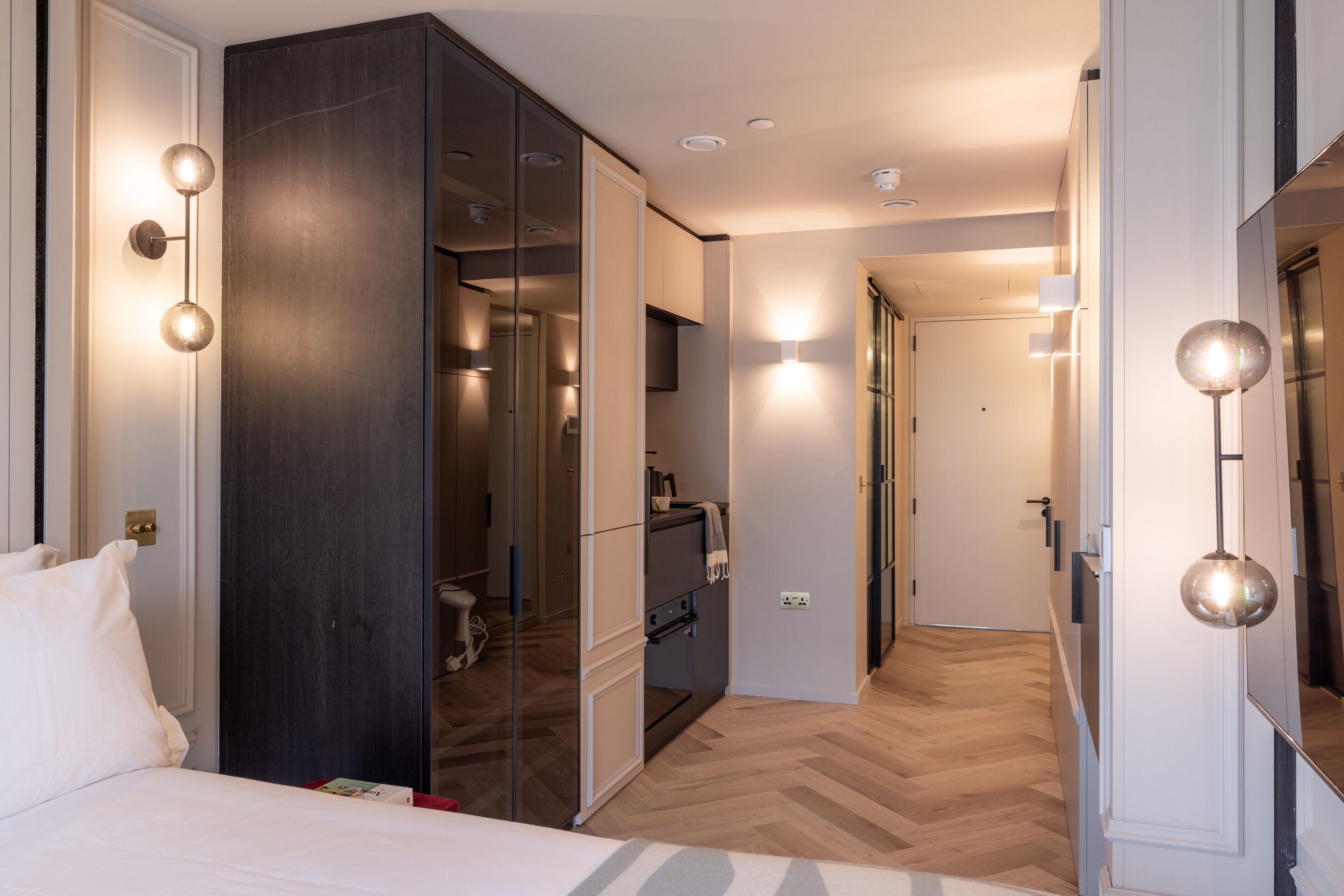 A modern hotel room with a large bed, a wardrobe, a mirror, and a bathroom visible through a glass partition.