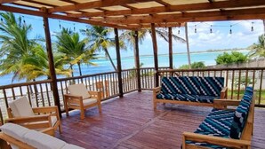 A wooden deck with a view of the ocean, featuring wooden chairs and a sofa.