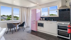 A modern kitchen with a pink refrigerator, white cabinets, a gas stove, and a view of the neighborhood. - Hicks Haven - Waikanae Beach Holiday Studio (Waikanae)