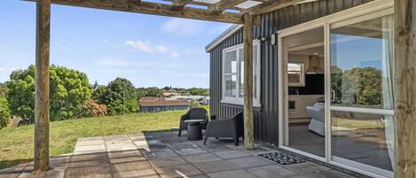 A covered patio with a view of a house, a grill, and outdoor seating.