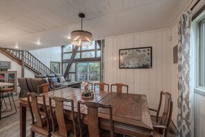 Un vaste espace dédié à la salle à manger, avec une grande table et des chaises en bois, un luminaire suspendu et un escalier menant à un niveau supérieur.