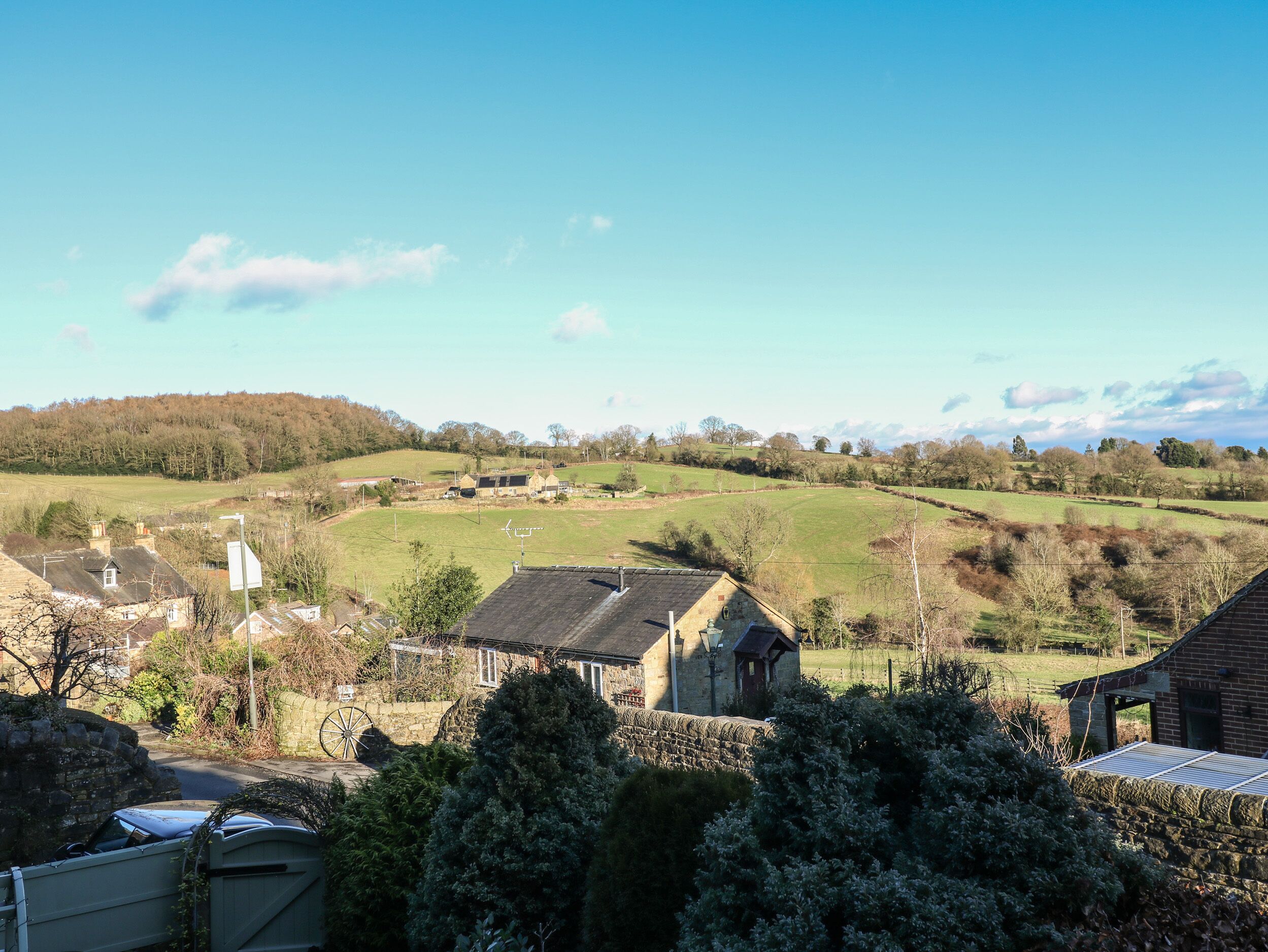 Ländliche Landschaft mit Steinhäusern, blauem Himmel und sanften Hügeln im Hintergrund.