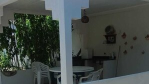 A covered outdoor seating area with a table and chairs, surrounded by greenery and a gravel path. - Recanto da Lua (Prado)