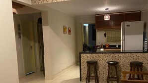 A spacious kitchen with a tiled floor, a central island with stools, and a refrigerator. - Recanto da Lua (Prado)