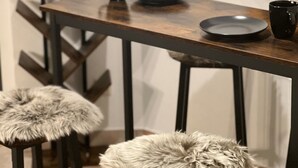 A modern bar area with a wooden table, two stools with fur cushions, and black mugs and plates.