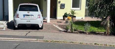 Een huis met twee verdiepingen, voorzien van een pannendak, een auto op de oprit en een kleine tuin.
