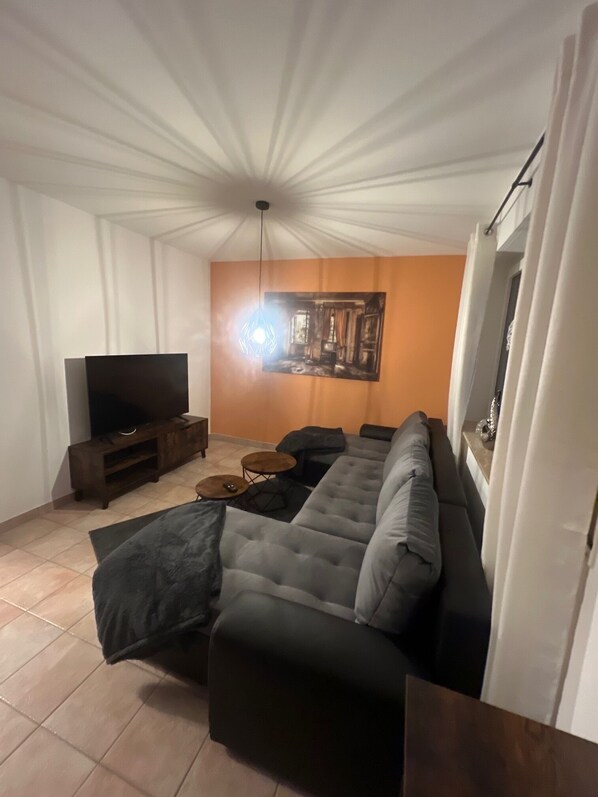 Un salón con un sofá modular, un televisor de pantalla plana, una mesa de centro y un cuadro en la pared.