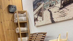 A wooden sauna bench, a wooden shelf with towels, a sauna heater, and a bucket with a spoon on a wooden table.