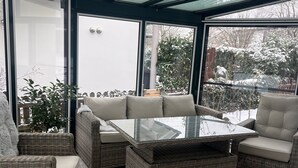 A sunroom with wicker furniture, a glass table, and a view of a snowy garden.