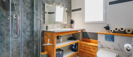 A modern bathroom with a glass-enclosed shower, a wooden vanity, a marble-tiled floor, and a toilet.
