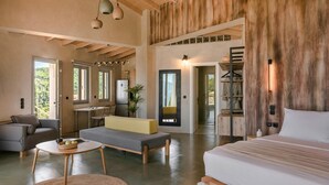 A spacious living area with a sofa, a dining table, and a bed. There is a kitchen area with a refrigerator and a dining table. The room has large windows and a view of the outdoors. - Villa Eugenia Sunrise (Kefalonia)