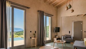 A spacious room with large sliding glass doors leading to a balcony with a view of a beach and mountains. - Villa Eugenia Sunrise (Kefalonia)