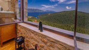 A room with a stone wall, a wooden desk, a chair, and a view of a mountainous landscape through large windows. - Villa Bolios Sea View Private Pool (Kefalonia)