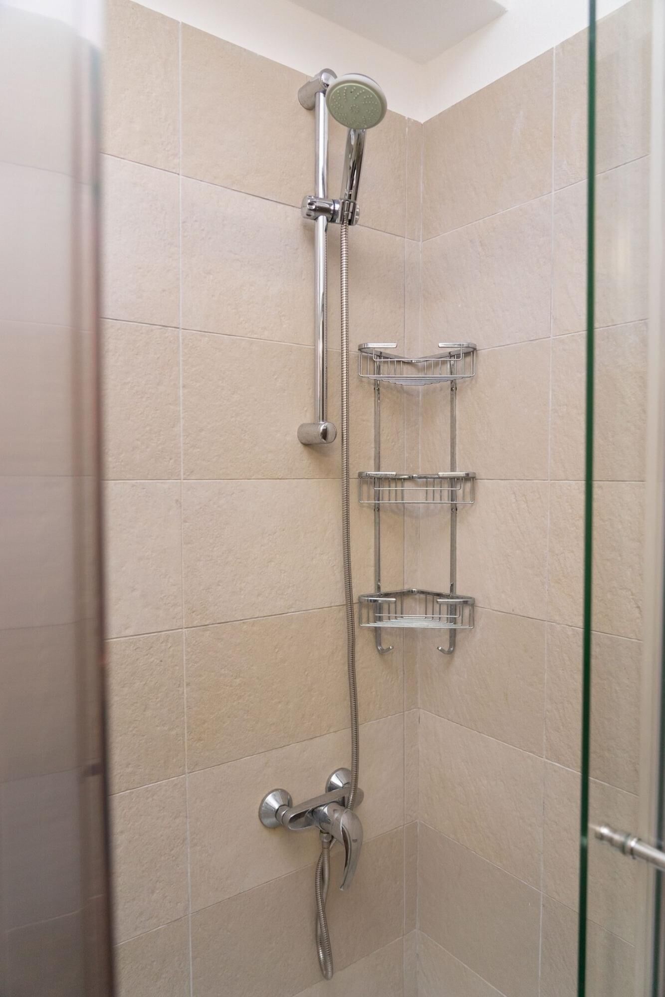 A shower with a handheld showerhead, a wall-mounted faucet, and a glass-enclosed shower area.