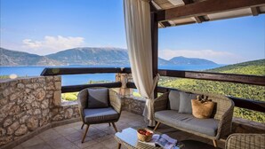 A balcony with wicker furniture, a stone wall, and a view of a lake and mountains. - Villa Bolios Sea View Private Pool (Kefalonia)
