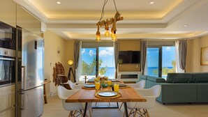 A modern kitchen with a stainless steel refrigerator, a dining table set for four, and a view of the sea through large windows.