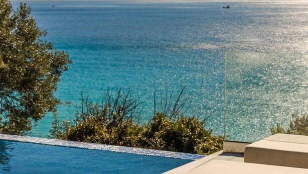 A poolside area with a clear view of the sea and mountains in the background.