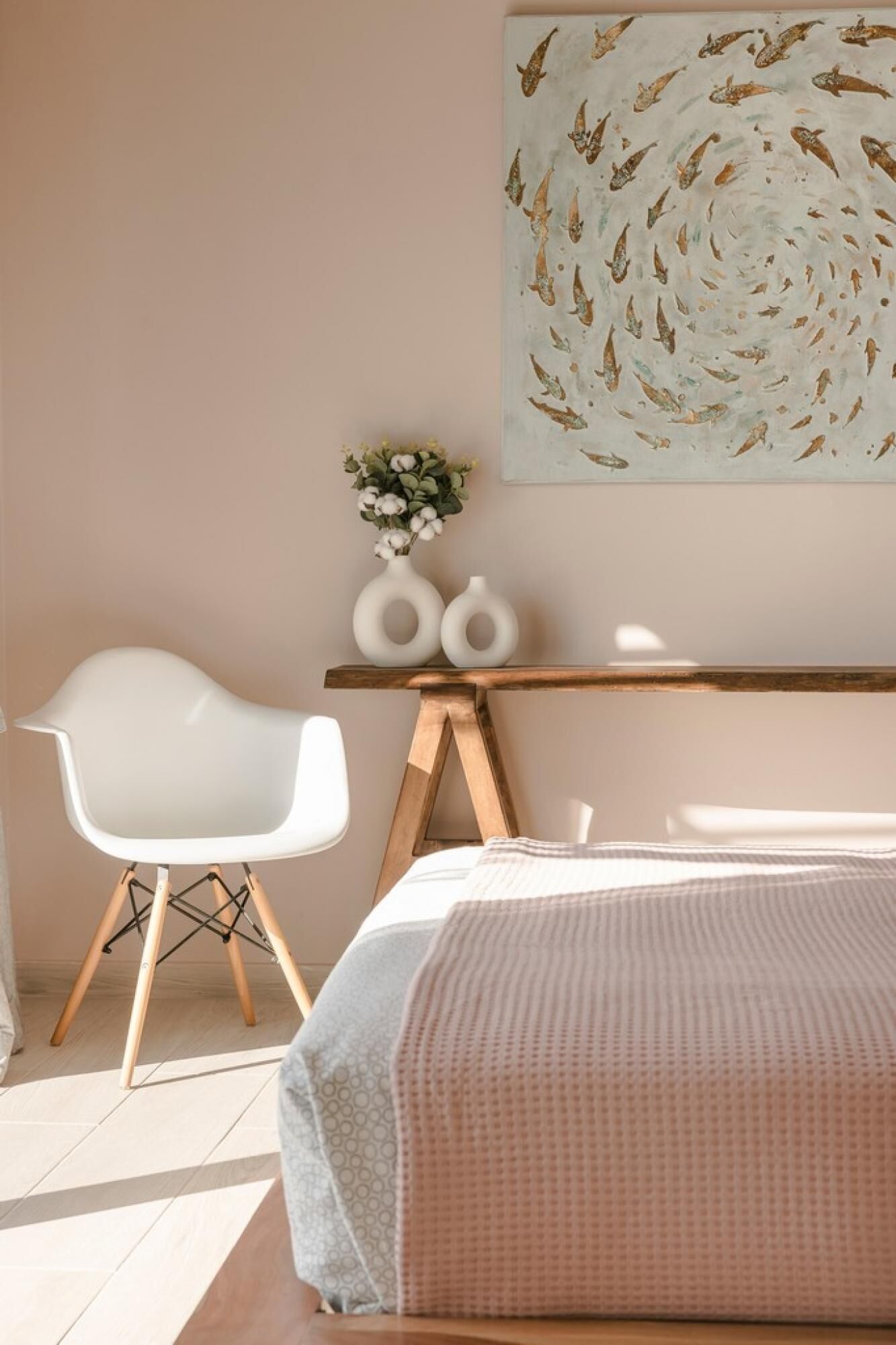A bedroom with a bed, a white chair, a wooden desk, and a wall-mounted artwork.