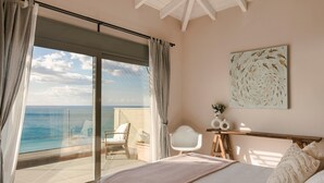 A bedroom with a large sliding glass door leading to a balcony with a view of the sea.