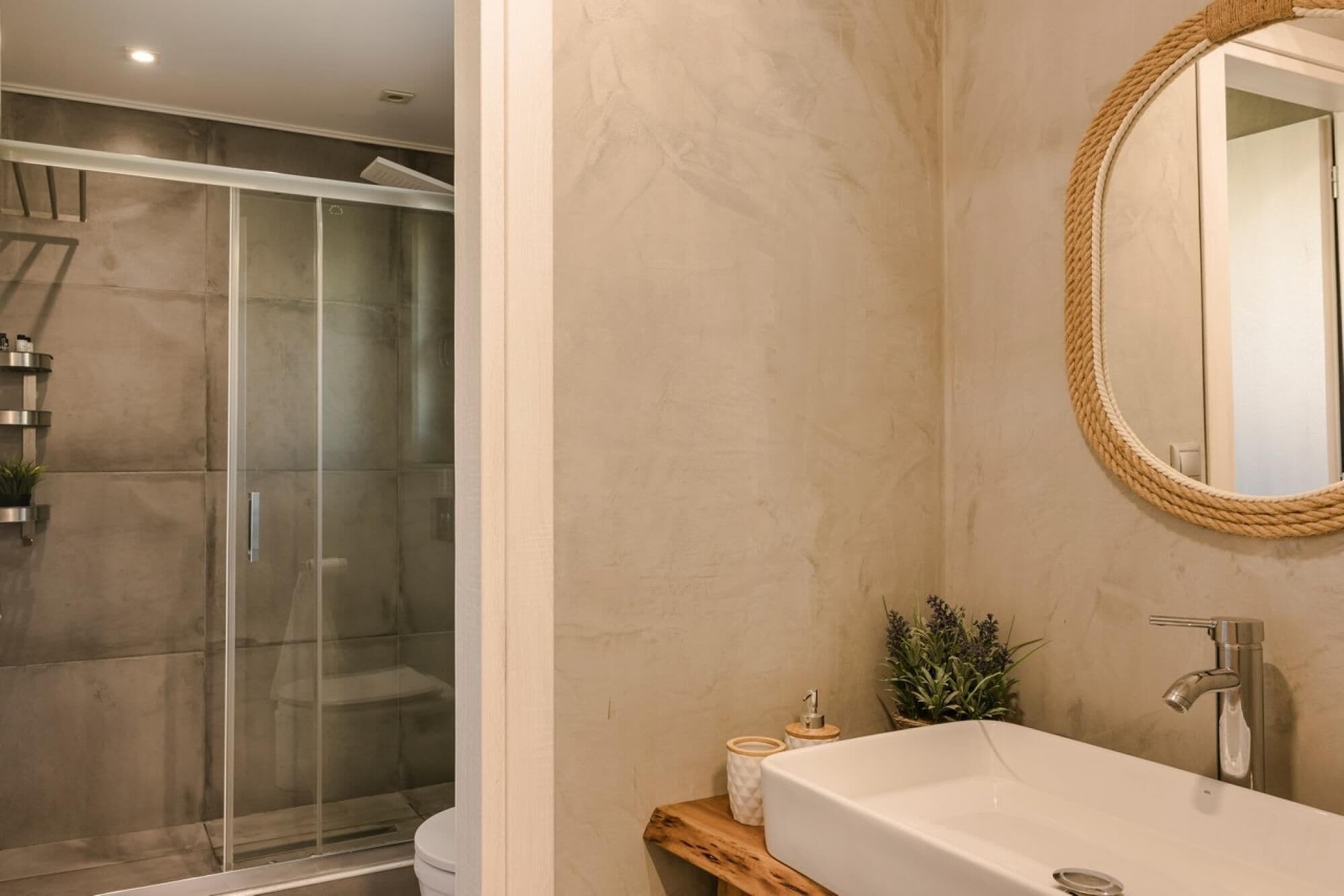 A bathroom with a glass-enclosed shower, a wooden vanity, a large mirror, and a white sink.