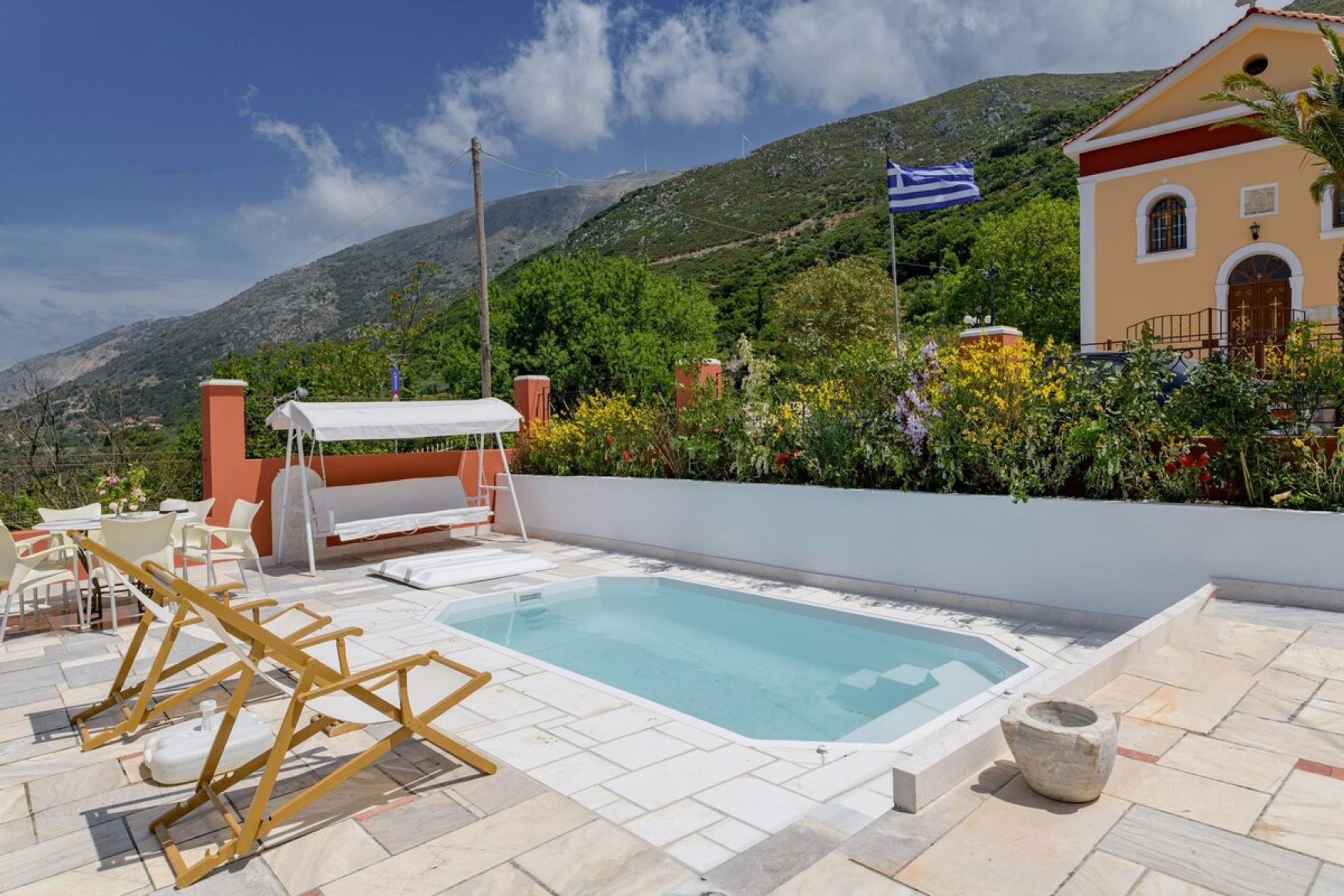 A swimming pool with a white deck, surrounded by a white wall and a mountain backdrop.