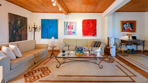 Una sala de estar con techo de madera, un sofá color beige, una mesa de centro de vidrio y un tapete con diseños geométricos.