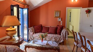 A cozy living room with a sofa, a coffee table, and a lamp. There is a door leading to another room and a window with curtains. - Entheos City Panorama Argostoli (Kefalonia)