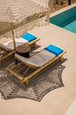 Uma área na piscina com duas espreguiçadeiras, uma mesa redonda e um guarda-sol de macramé.