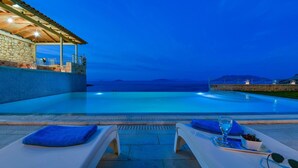 An infinity pool with a view of the sea, lounge chairs, and a covered area with a stone wall. - Infinite Blue Epidavros (Epidaurus)