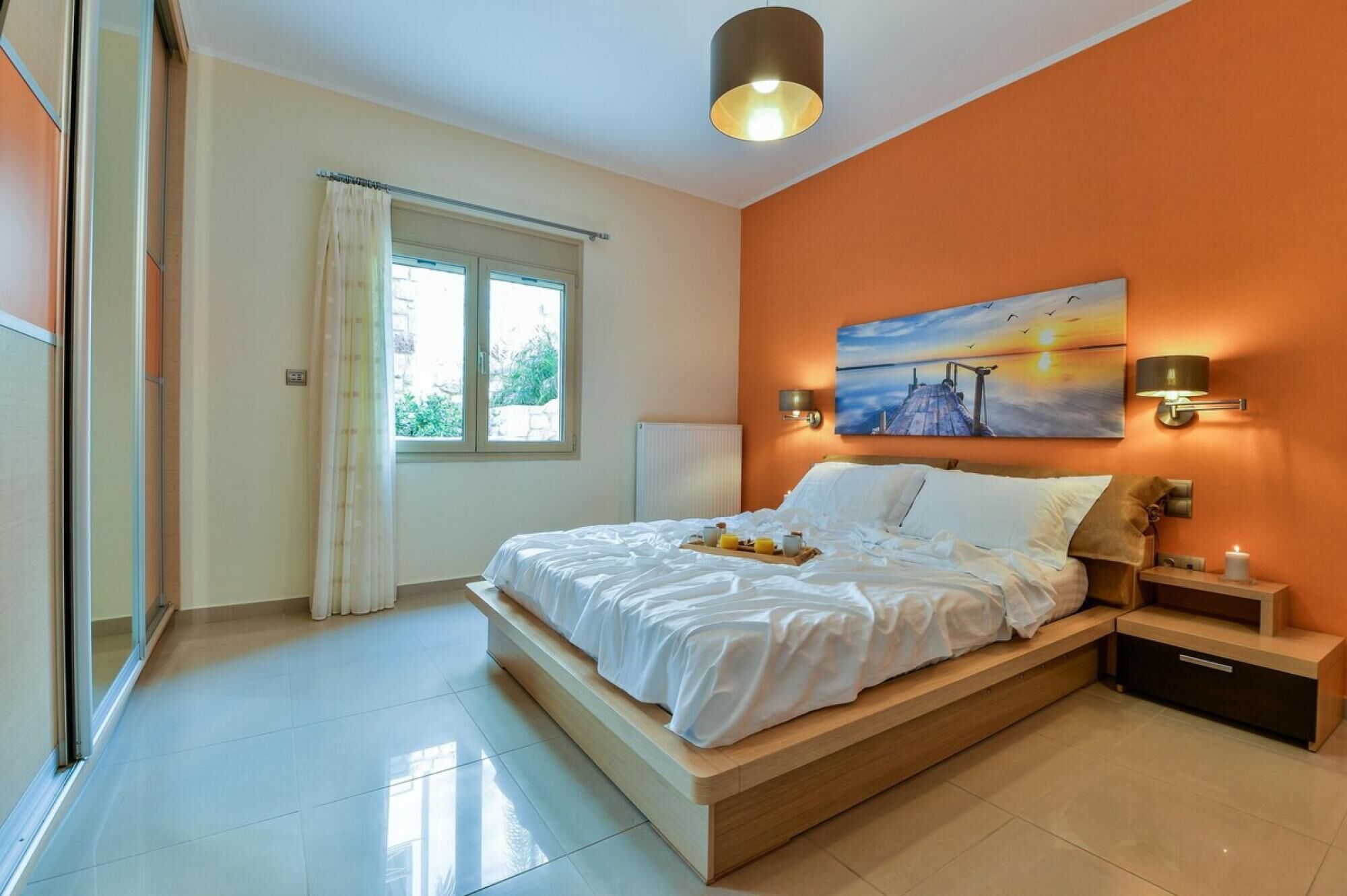 Une chambre à coucher avec un lit, des tables de chevet, un tableau et une fenêtre avec des rideaux.