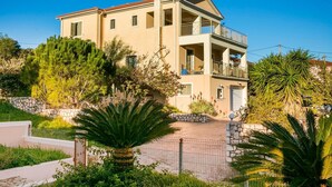 A two-story building with a stone wall, a balcony, and a garden with palm trees. - Belle Helens Villa Kefalonia (Kefalonia)