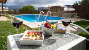 A poolside table with two glasses of red wine, a bowl of fruit, and a tray of snacks. - Belle Helens Villa Kefalonia (Kefalonia)