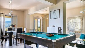 A pool table in a room with a dining area, a radiator, and a window with curtains. - Belle Helens Villa Kefalonia (Kefalonia)
