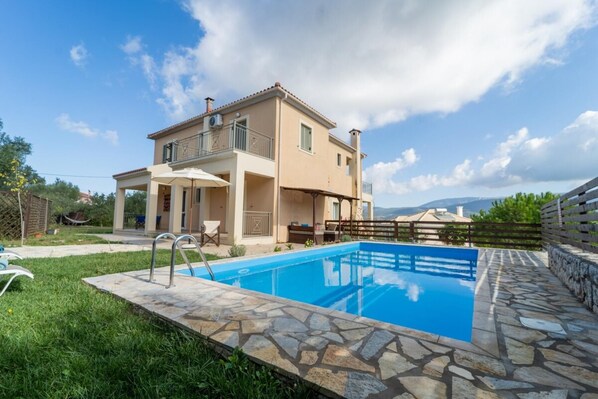 A two-story house with a swimming pool, stone patio, and a view of the mountains.