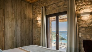 Ein Schlafzimmer mit Bett, Holzwänden, Steinwänden und Blick auf Pool und Berge.