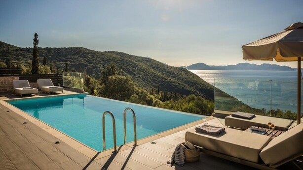 Ein Pool mit klarem, blauem Wasser, Liegestühlen und Blick auf eine gebirgige Landschaft mit einem Gewässer in der Ferne.