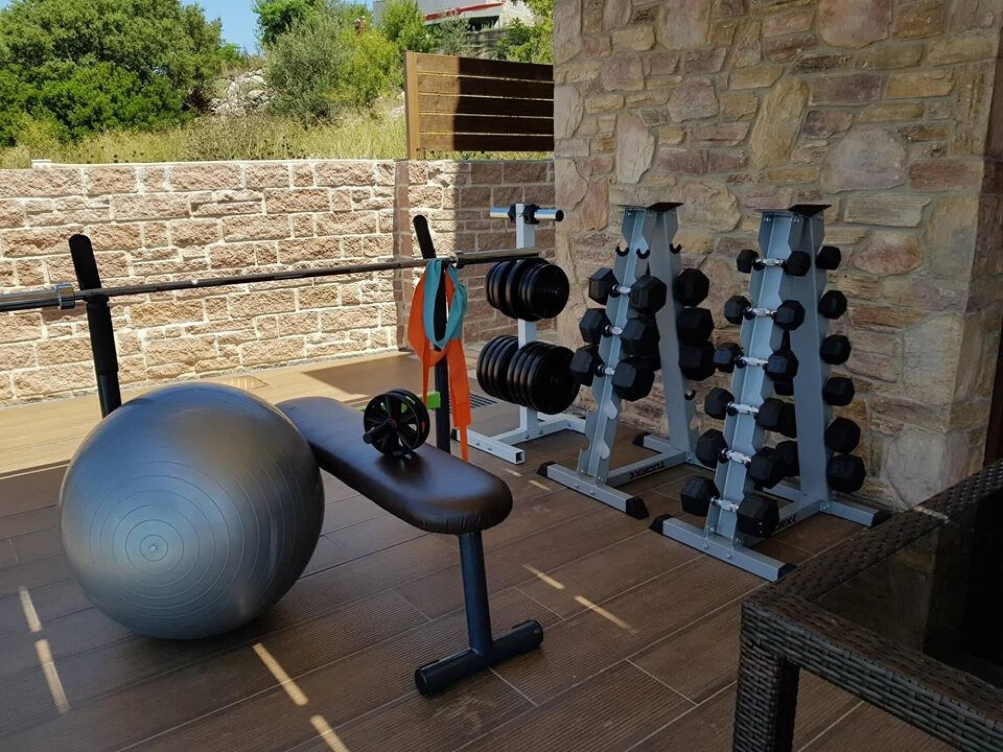 Un gimnasio con equipo de ejercicios, incluyendo una banca, una pelota medicinal y estantes para pesas.