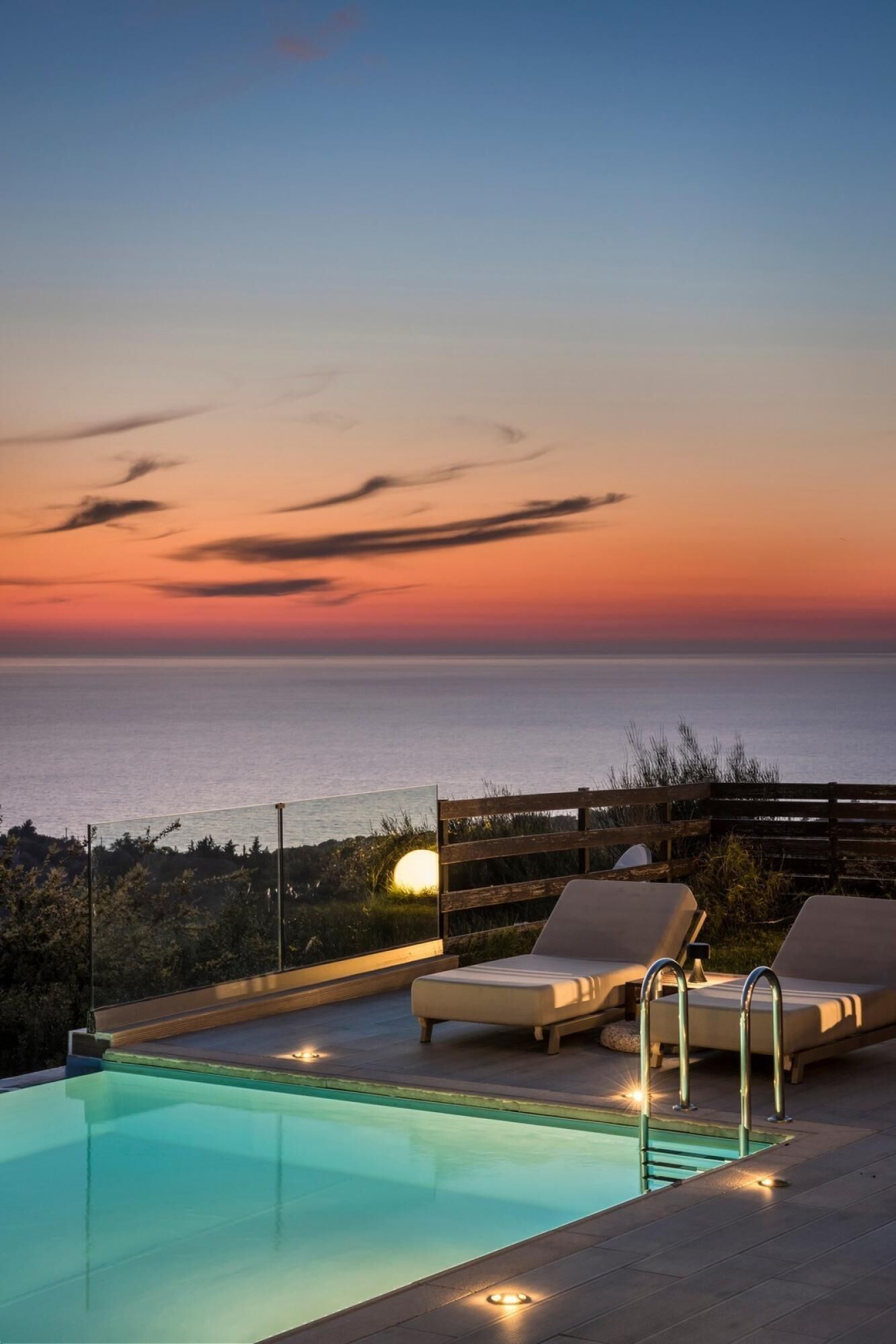 Une piscine sur le toit, avec deux chaises longues et une vue sur l’océan au coucher du soleil.