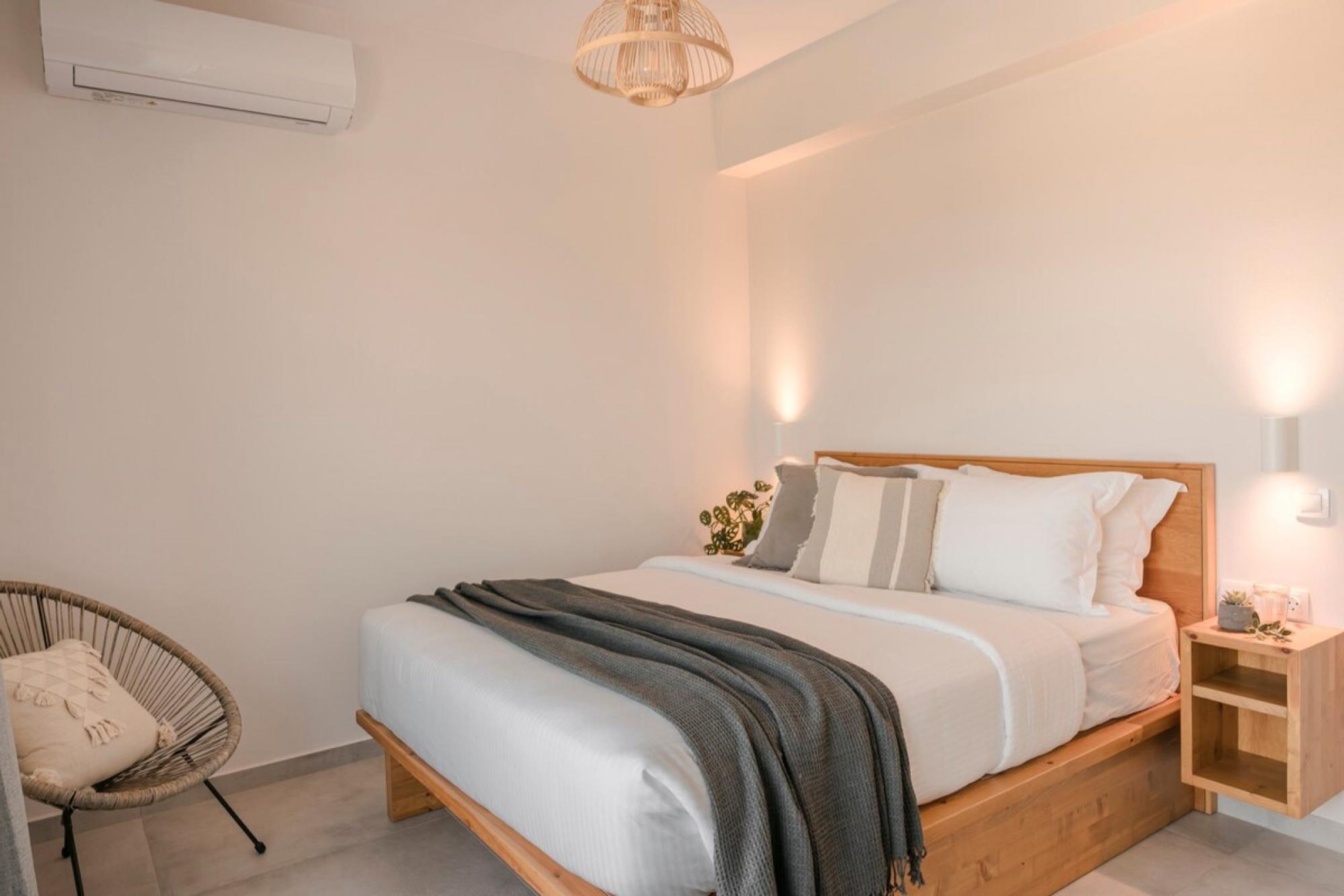 Un dormitorio moderno con una cama de madera, una silla de mimbre y una mesita de noche con una lámpara.